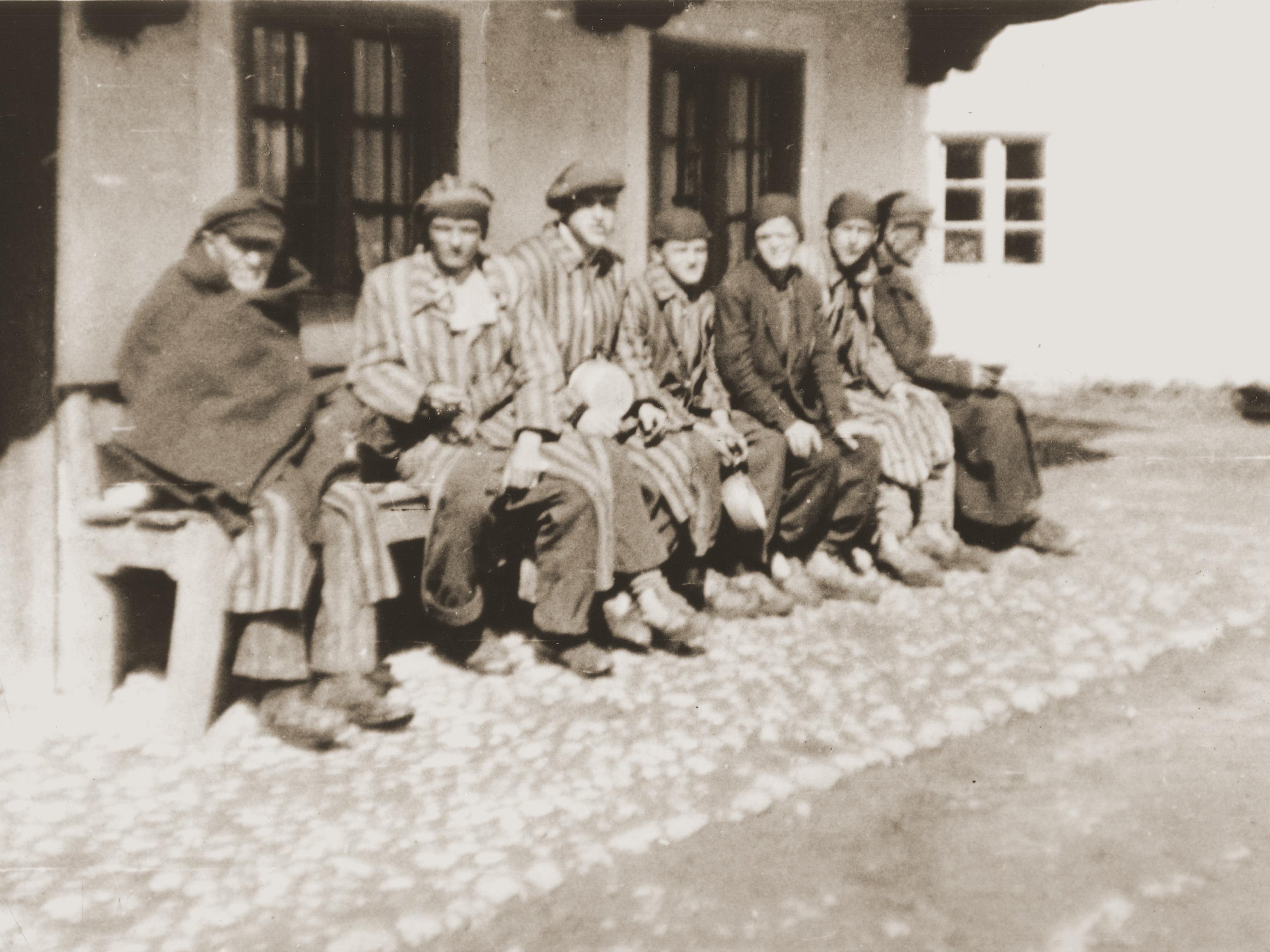 Eine Gruppe von KZ-Häftlingen, die auf einem Todesmarsch aus Dachau befreit wurden, sitzen auf einer Bank und warten darauf, von japanisch-amerikanischen Soldaten des 522nd Field Artillery Battalion etwas zu essen zu bekommen.