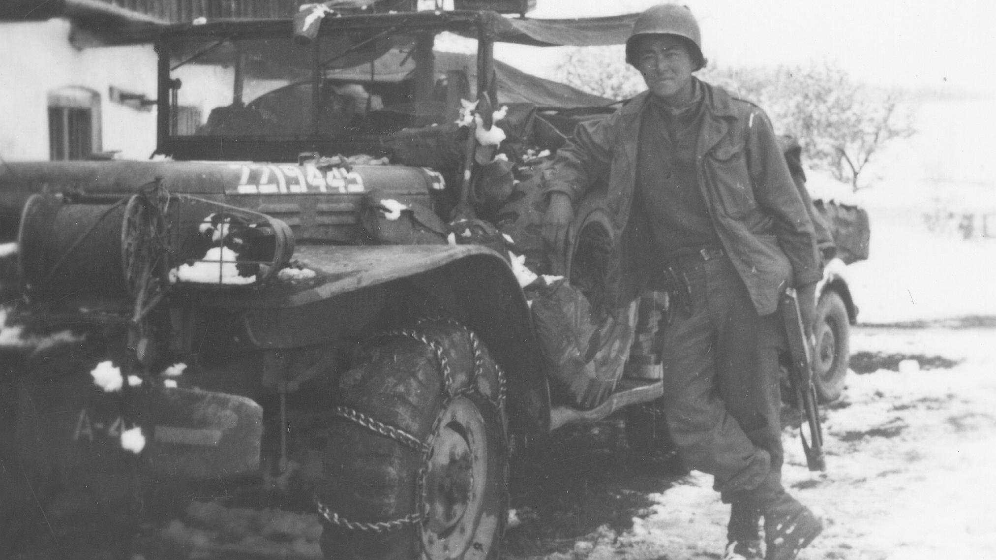Ein japanisch-amerikanischer Soldat posiert neben seinem Jeep in der Gemeinde Waakirchen, wo das 522nd Field Artillery Battalion ein provisorisches Feldlazarett für Überlebende des Todesmarsches von Dachau einrichtete.
